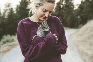A woman, smiling, is looking down at a kitten which she is holding in her arms.