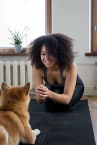 A smiling and laughing woman in workout gear is leaning forward, playing with her dog.
