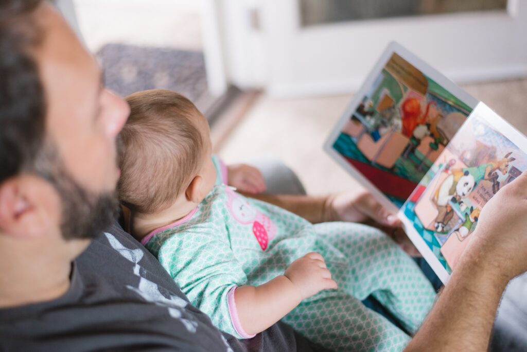 A father is reading a book to his baby/toddler